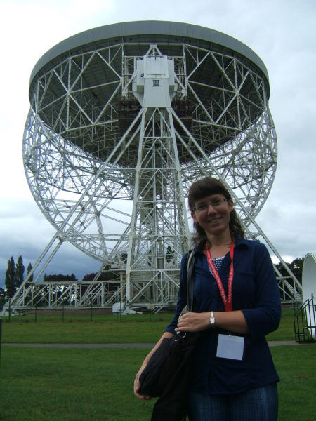 Kobieta z identyfikatorem na szyi przed radioteleskopem.